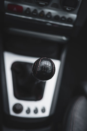 Black leather gear knob of a manual gearbox car. Interior shot, selective focus, no people.