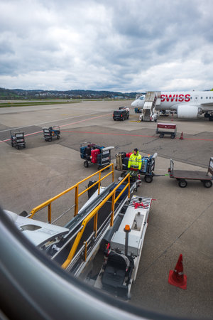 Commercial airplane luggage handlers loading baggage onto a Swiss Air plane on 04/03/2023.のeditorial素材