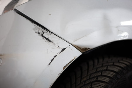Scratched and dented paint and car bodywork. Close up shot of silver painted car bumper, wheel arch,...
