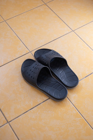 A pair of rubber or plastic mens slipper on the tile floor of an apartment bathroom. Top view, close...