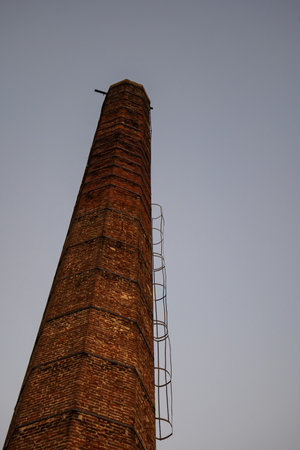 Old, run down, decaying, tall brick chimney of an abandoned urban power plant at dusk, no people.の写真素材