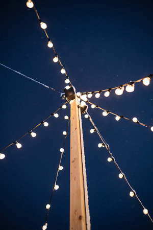 Decorative string lights hanging from a wooden pole. Tungsten light bulbs, dark blue sky, low angle...