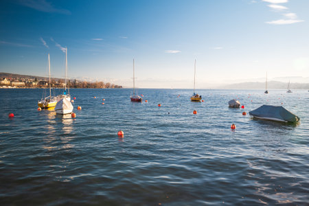 Small sail boats floating on lake Zurich in the autumn surrounded by buoys. Sunny afternoon light, no people.の写真素材