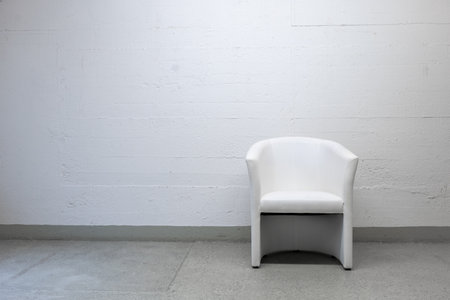Old vintage, well-used white leather armchair set against grungy concrete wall, no people.の写真素材