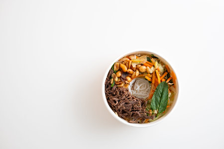 Cardboard bowl of take out Asian ramen noodles with pulled beef, rice noodles and cooked vegetable....