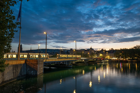 03-09-2024 Zurich, Switzerland. QuaibrÃ¼cke or Quai bridge over the Limmat river at sunrise. Light bridge traffic, trams, dramatic sky, reflections in the water.のeditorial素材