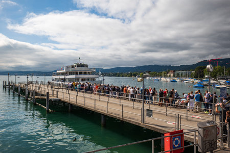 06-09-2024 Zurich, Switzerland. Linth tourist cruise ship docking at Burkliplatz pier to take passengers onboard. Sunny summer day, crowds of tourists queuing.のeditorial素材