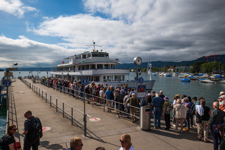 06-09-2024 Zurich, Switzerland. Linth tourist cruise ship docking at Burkliplatz pier to take passengers onboard. Sunny summer day, crowds of tourists queuing.のeditorial素材
