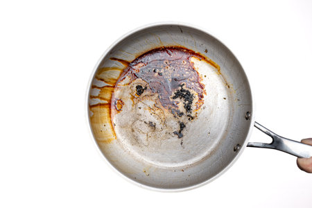 Dirty, oil and grease burnt bits and stains on a metal frying pan. Held in hand by male hand. Close up studio shot, isolated on white.の写真素材