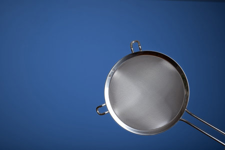 Stainless steel sieve. Close up studio shot, isolated on blue.