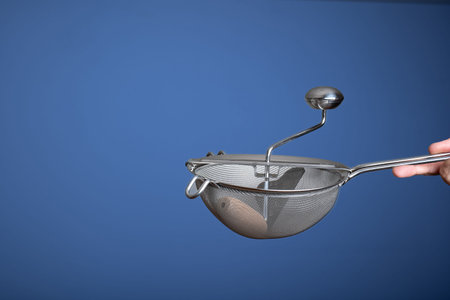 Stainless steel sieve with crank. Held by hand by Caucasian male hand. Close up studio shot,...