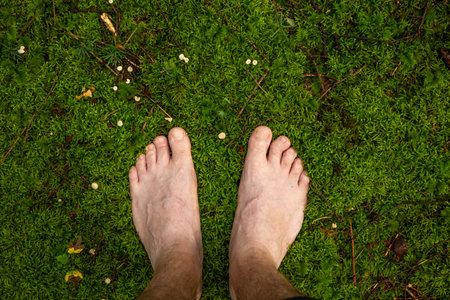 Caucasian adult's bare feet standing on mossy forest ground. Close up shot, unrecognizable person,...