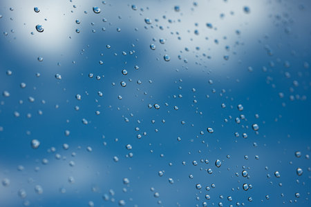 Water droplets on glass window. Blue sky and white clouds in the background, close up macro shot.の写真素材