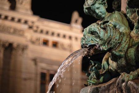 Old, weathered, bronze gargoyle water fountain statue head with water streaming from the mouth. Close up, night shot, shallow depth of field, no people.の写真素材