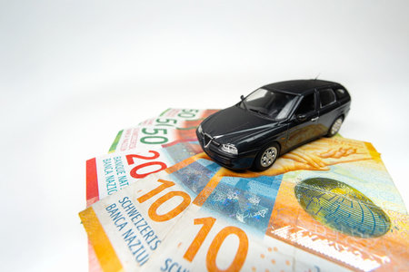Small metal toy model car on a spread stacks of 10, 20 and 50 banknotes. Upper side view, distorted ultra-wide-angle view, close up, isolated on white, no people.の写真素材