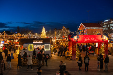3-12-2024 Zurich, Switzerland. People visiting pop-up shops at the Sechselautenplatz Christmas market. Blue hour late evening, Christmas lights.のeditorial素材