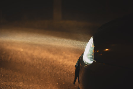 Car headlights illuminating the water particles of a thick winter fog on an empty road at night. Close up, moody shot, no people.の写真素材