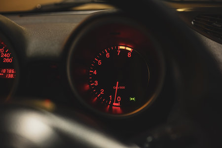 Car's round rev counter gauge illuminated at night. Close up shot, illuminated red line indicator,...