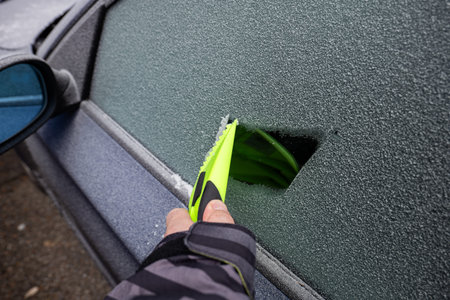 Male hand using a plastic ice scrapper on a frozen car window in the morning. Close up shot.