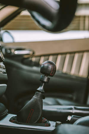 Car interior manual gearbox shifter lever with black leather gear knob. Low angle, close up shot, no...