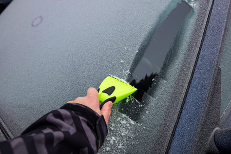 Male hand using a plastic ice scrapper on a frozen car window in the morning. Close up shot.