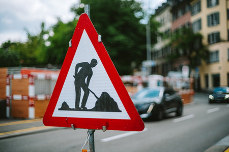 Road works ahead triangle road sign. Close up shot, shallow depth of field, daytime, blurred city scene in the background, blurry car driving byの写真素材