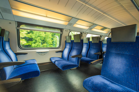 Empty blue cloth seats inside passenger train in Europe. Large window side seats, moving train,...