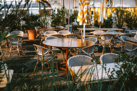 Folded and closed large outdoor umbrellas, tables and chairs in street eatery or cafe in Europe. Sunny summer morning before opening time, no peopleの写真素材
