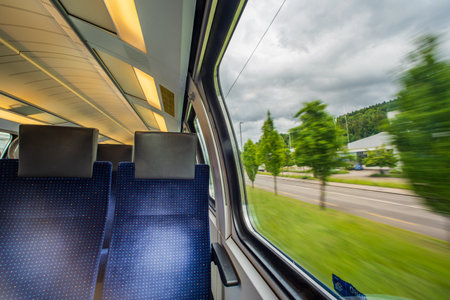 Empty blue cloth seats inside passenger train in Europe. Large window side seats, moving train, blurred exterior rural  background, no people.の写真素材