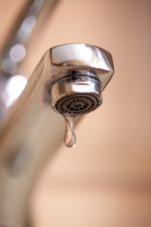 Dripping tap with water droplets inside apartment bathroom. Macro, close up, looking up shot, shallow depth of field, no peopleの写真素材