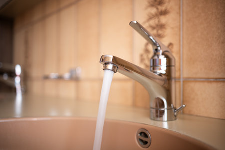 Shiny, chrome tap with running water stream inside apartment bathroom. Close up shot, shallow depth of field, no peopleの写真素材