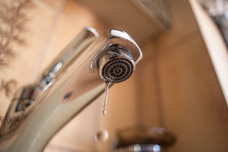 Dripping tap with water droplets inside apartment bathroom. Macro, close up, looking up shot, shallow depth of field, no peopleの写真素材