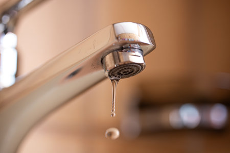 Dripping tap with water droplets inside apartment bathroom. Macro, close up, looking up shot, shallow depth of field, no peopleの写真素材