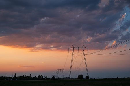 High voltage power line tower pole in a field at sunset. Low, wide angle view, dramatic sunset...