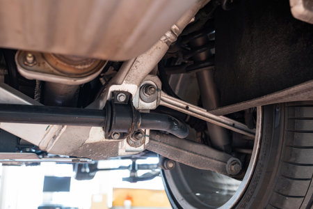 Car rear axel assembly with control arm, coil spring, shock absorber and stabilizer bar. Wide angle, looking up shot of a lifted car in a repair shot, no peopleの写真素材