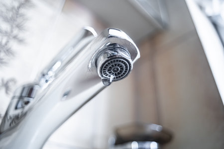 Dripping tap with water droplets inside apartment bathroom. Macro, close up, looking up shot,...