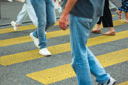 Unrecognizable legs of people crossing a yellow zebra or urban pedestrian crossing. Waist down view of people, legs and feet on asphalt crossing, sunny summer dayの写真素材