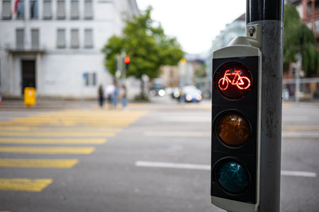 Bicycle traffic light next to pedestrian crossing, showing red. Close up, wide angle shot, shallow depth of field, blurry background and peopleの写真素材