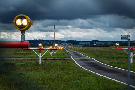 Precision Approach Path Indicator lights in front of an empty airport runway strip and edge lights. Close up shot of the light clusters, dark, moody, cloudy atmosphere, no peopleの写真素材