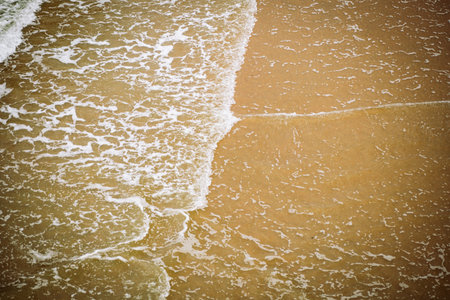 Foamy, shallow, tidal waves reaching the sandy shore. Top down view, shallow water, orange warm...