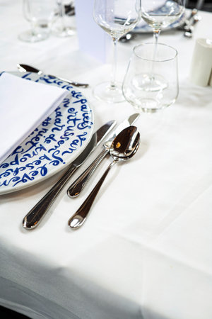 Empty, delft blue decorated ceramic dinner plate and silver cutlery arranged on a white table cloth....
