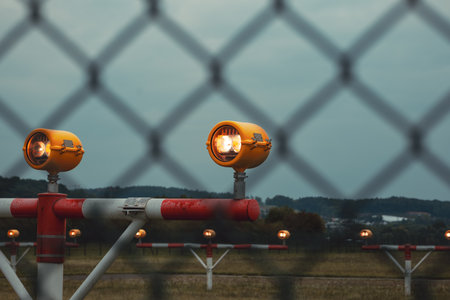 Precision Approach Path Indicator lights in front of an empty airport runway strip and edge lights. Close up shot of the light clusters, dark, moody, cloudy atmosphere, no peopleの写真素材