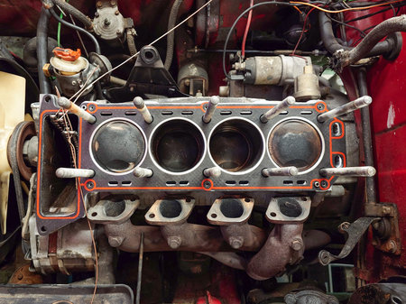 Open, inline four engine block with head gasket, exposed cylinders with carbon deposits or buildup...