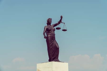 Statue of Justice with sword and scales in front of a blue cloudy skyのeditorial素材