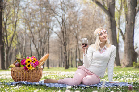 Beautiful teen blonde girl in park drinking red wineの写真素材