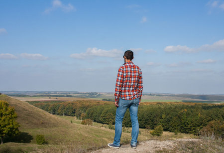 Young man standing on a hill enjoying beautiful scenery. Concept of travel and freedom.の写真素材