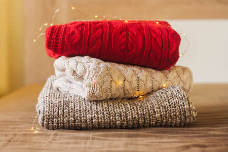 A pile of knitted sweaters on the wood bed decorated with lights. Warm comfortable clothes.の写真素材
