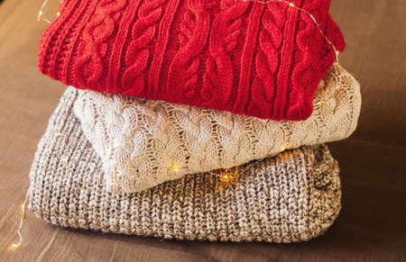 A pile of knitted sweaters on the brown tissue background decorated with lights. Warm comfortable clothes.の写真素材
