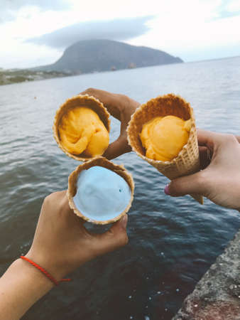 Ice cream cones in female hands against sea background. Moody summer picture.の写真素材
