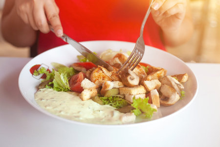 Female hands cutting delicious salad of chicken and vegetables and sauce with knife and fork at restaurant. Close up of a plate.の写真素材